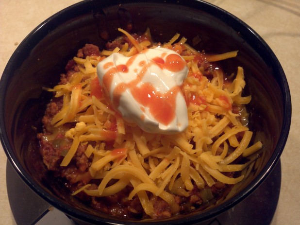 Caveman Chili topped with cheese, sour cream and frank's red hot